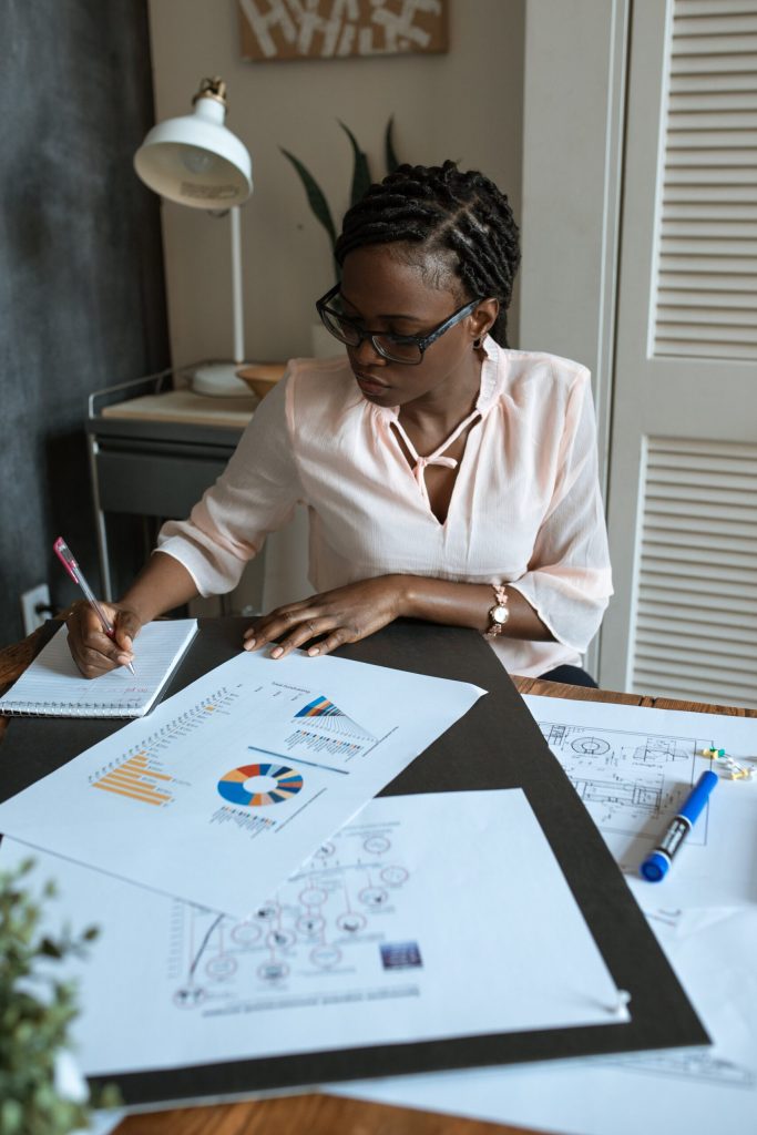 Woman Writing on Table With Charts